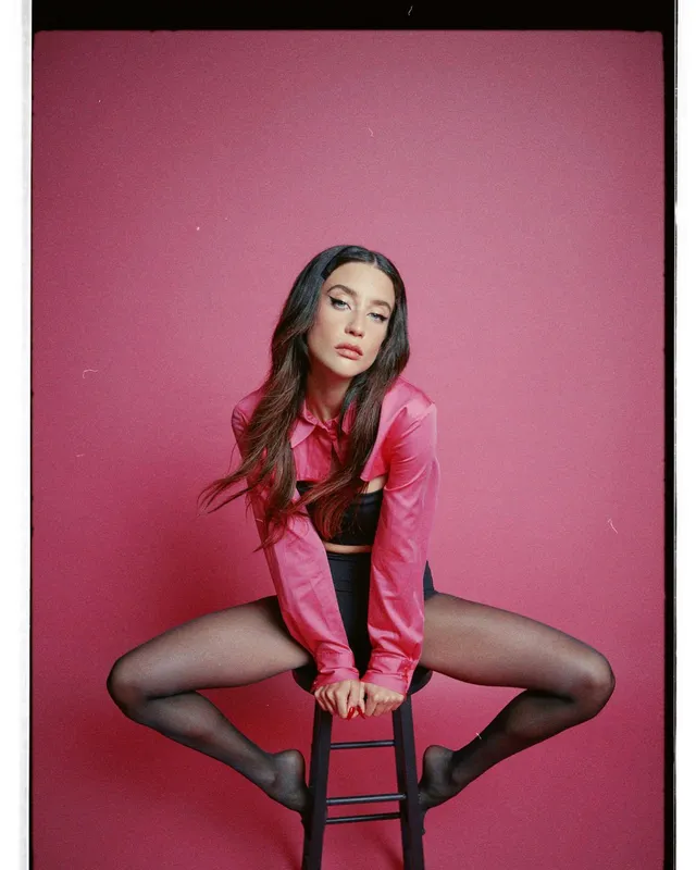 María Pedraza sitting on a stool in a pink blazer and dark tights for a portrait.