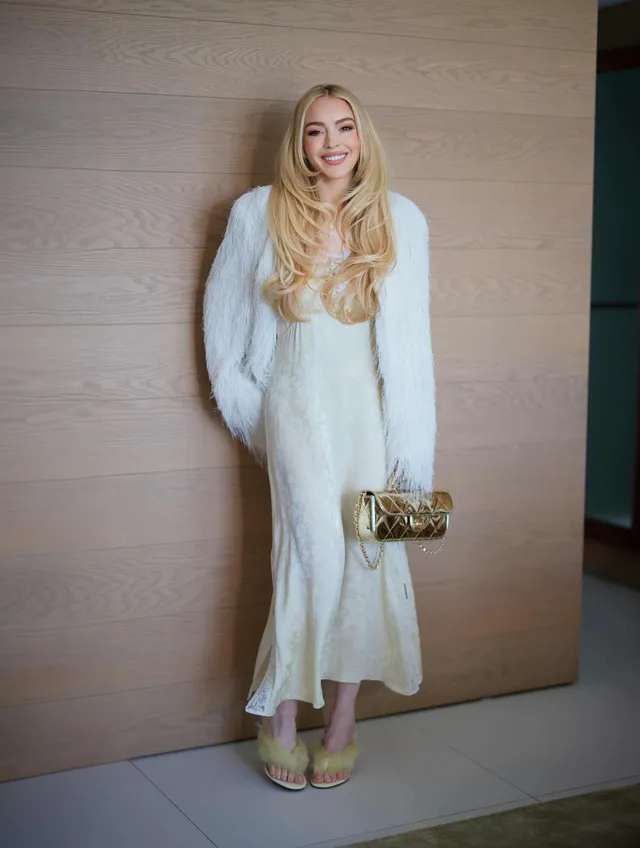 Lindsay Lohan posing in a white outfit and pale heels indoors.