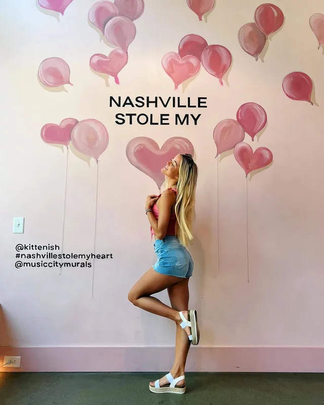 Olivia Dunne posing beside a mural in a pale top and shorts.