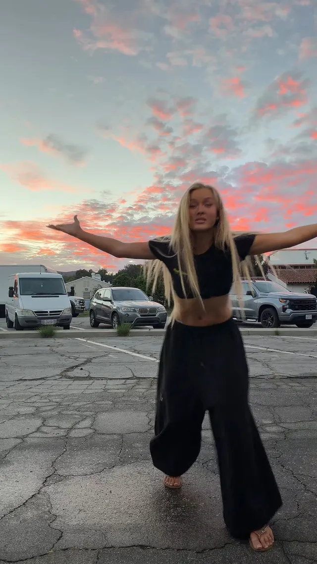 Zara Larsson standing barefoot outdoors beneath a sunset sky.