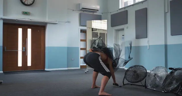 Naomi Scott crouching barefoot beside floor fans.