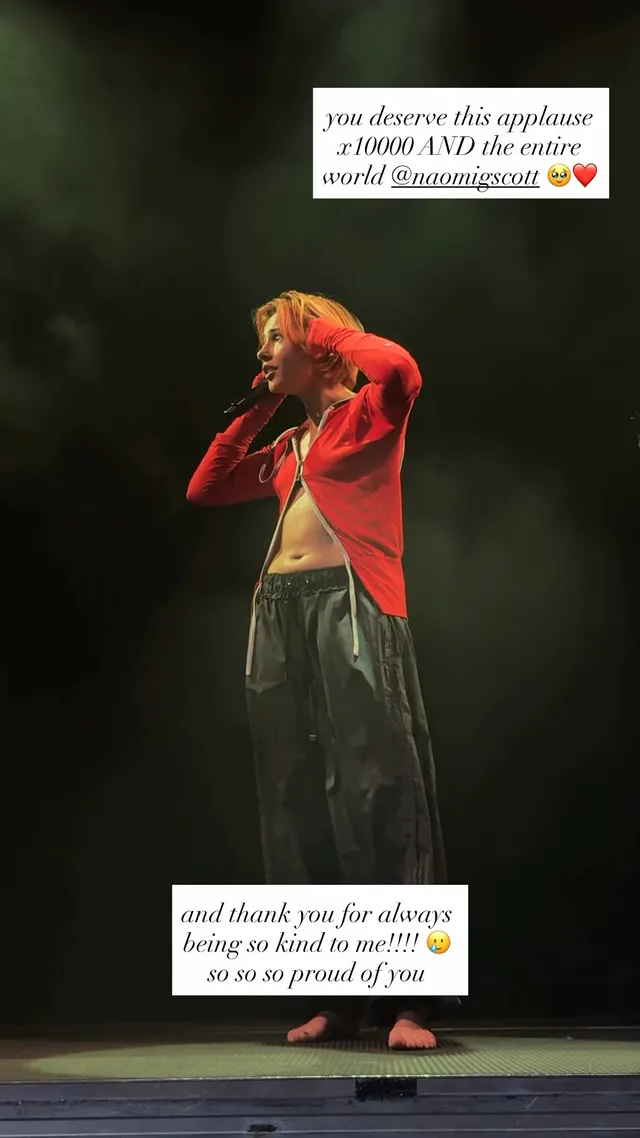 Naomi Scott singing barefoot in a red jacket onstage.