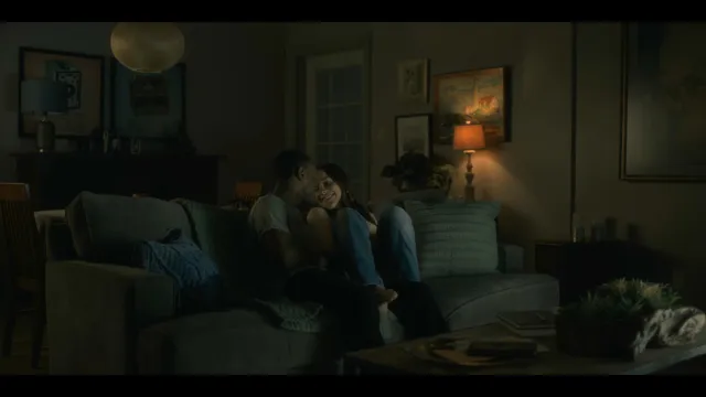 Victoria Pedretti sitting on a sofa with a companion during a screen scene.
