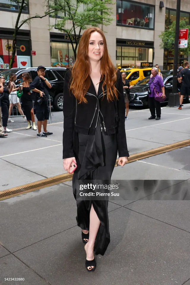 Karen Gillan walking outside in a dark outfit and black heels.