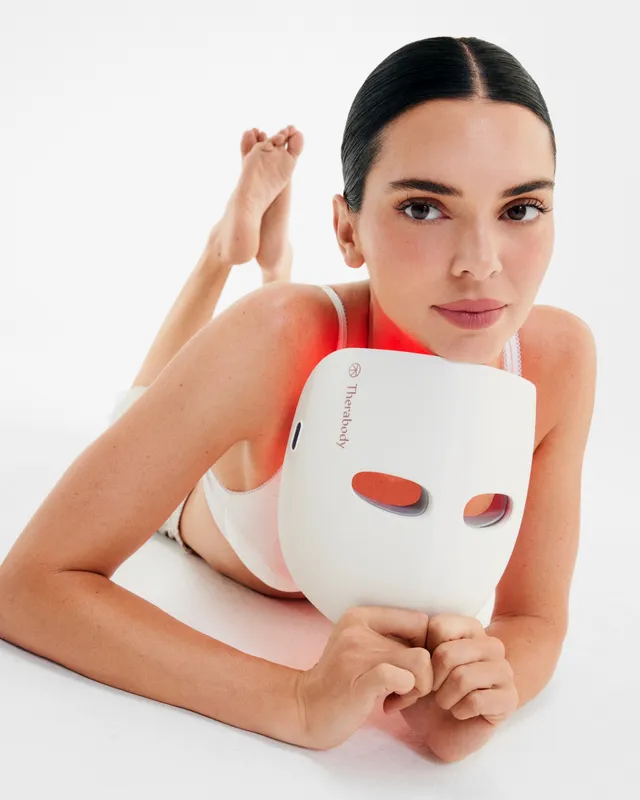 Kendall Jenner lying barefoot in a white studio holding a face mask.