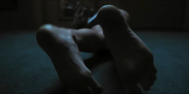 Alice Eve resting bare feet in a dimly lit scene.