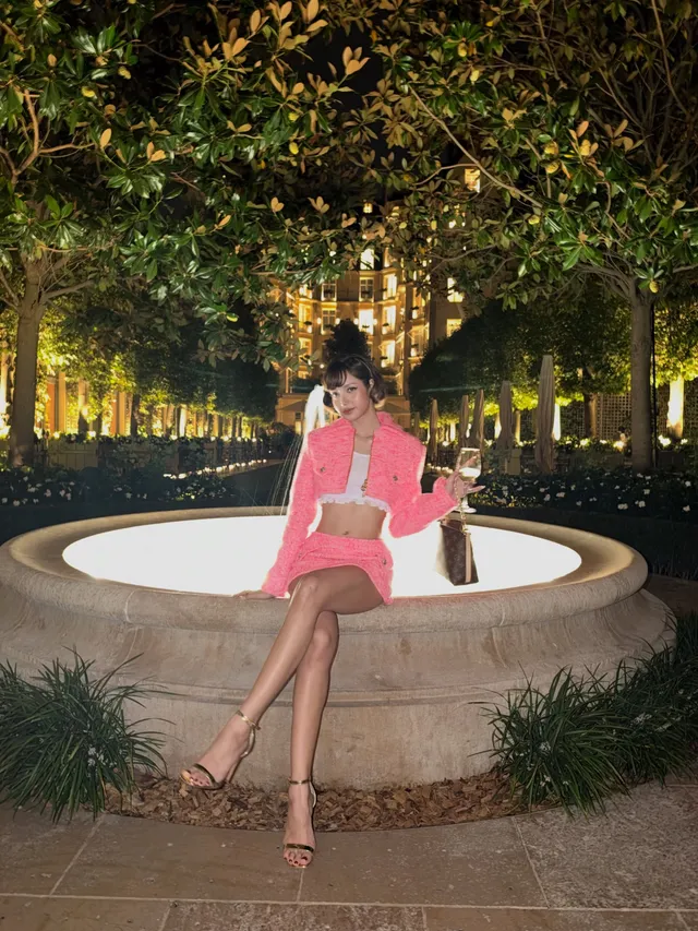 Lisa (Lalisa Manobal) sitting in gold heels and a pink outfit beside an illuminated garden feature.