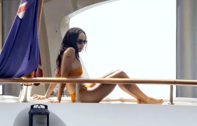 Zoë Kravitz sitting on a boat deck in a yellow swimsuit.