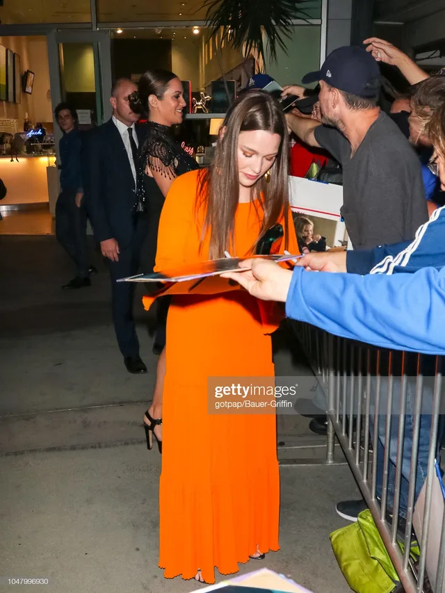 Victoria Pedretti standing beside event barriers in an orange dress.