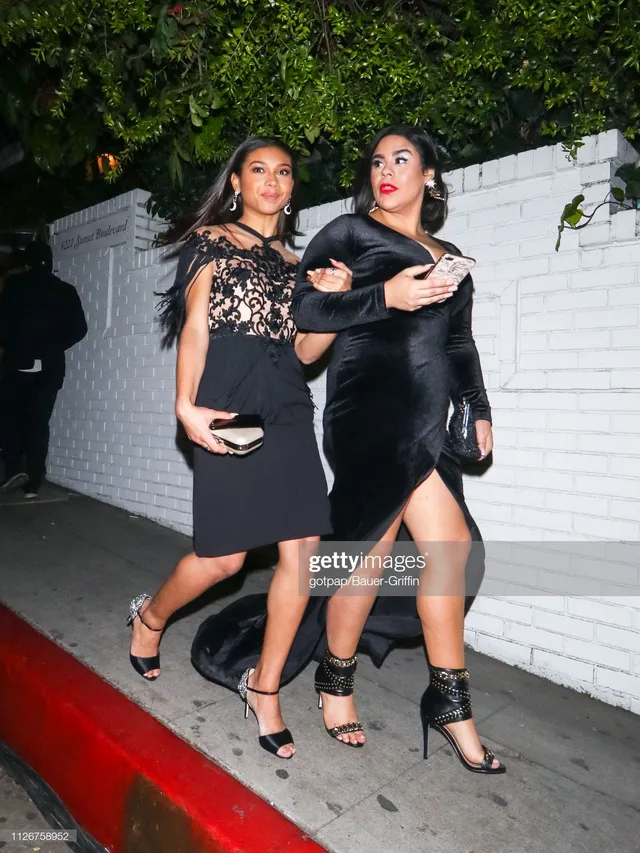 Sierra Capri walking beside a guest in a black lace outfit and heels.