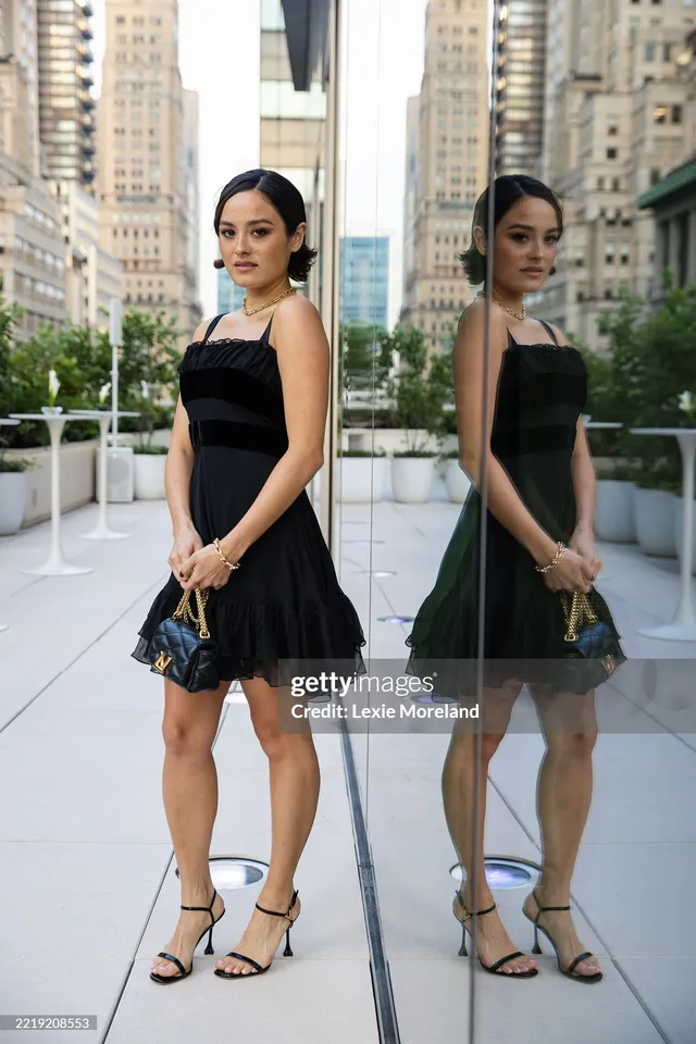 Chase Sui Wonders posing beside a mirror in a black dress and heels.