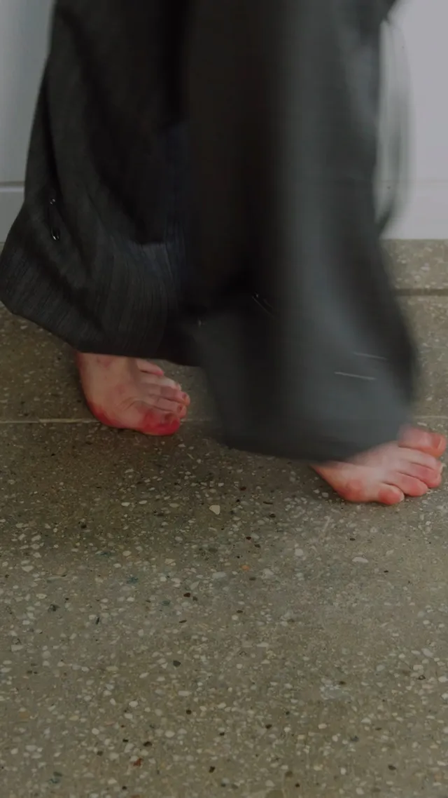 Sadie Sink showing bare toes beneath loose dark trousers.
