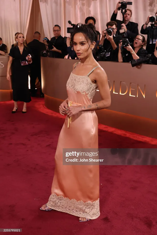 Zoë Kravitz posing on an awards carpet in a pale pink gown.