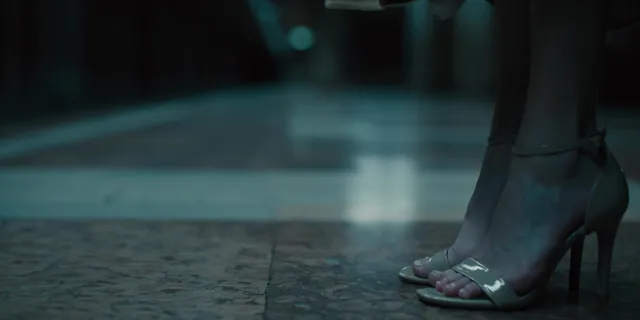 Maika Monroe wearing pale heels in a dimly lit scene.