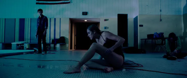Maika Monroe sitting barefoot on a tiled floor in a scene.