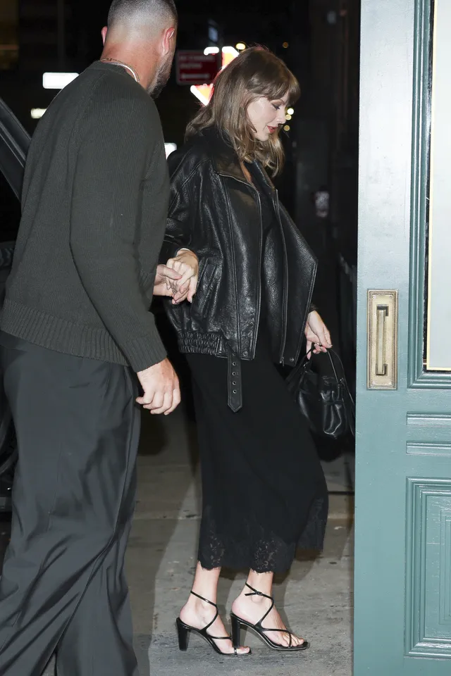 Taylor Swift leaving a building in a black outfit and heeled sandals.