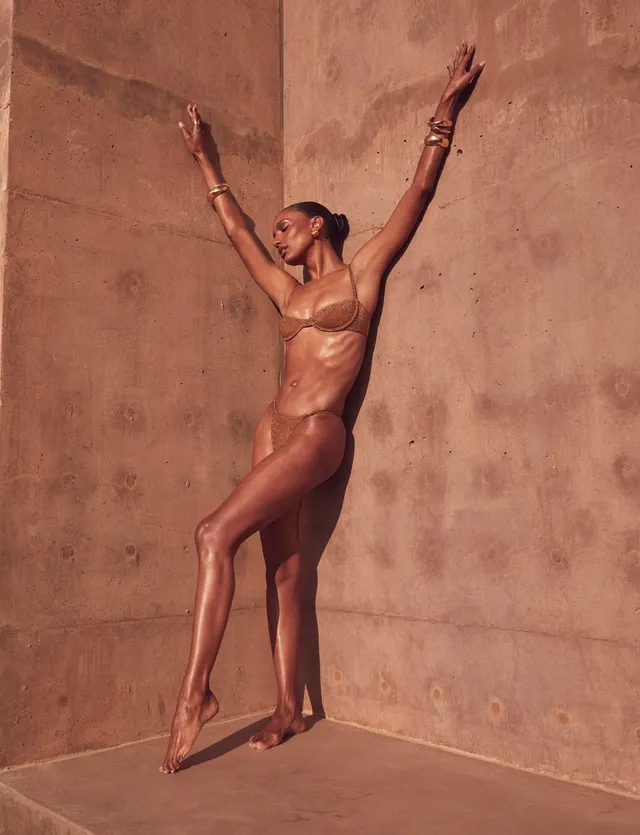 Jasmine Tookes balancing barefoot with her arms raised in a studio fashion portrait.