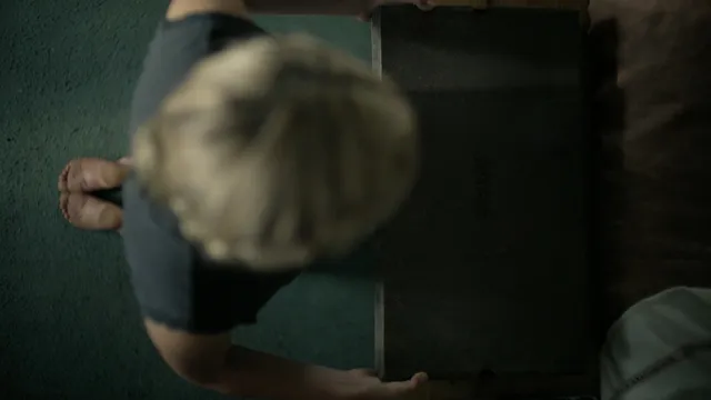 Kiernan Shipka standing barefoot on a carpet in a film scene.