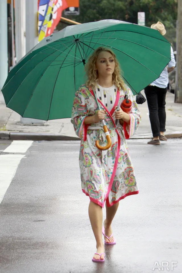 AnnaSophia Robb standing outdoors beneath a green umbrella.