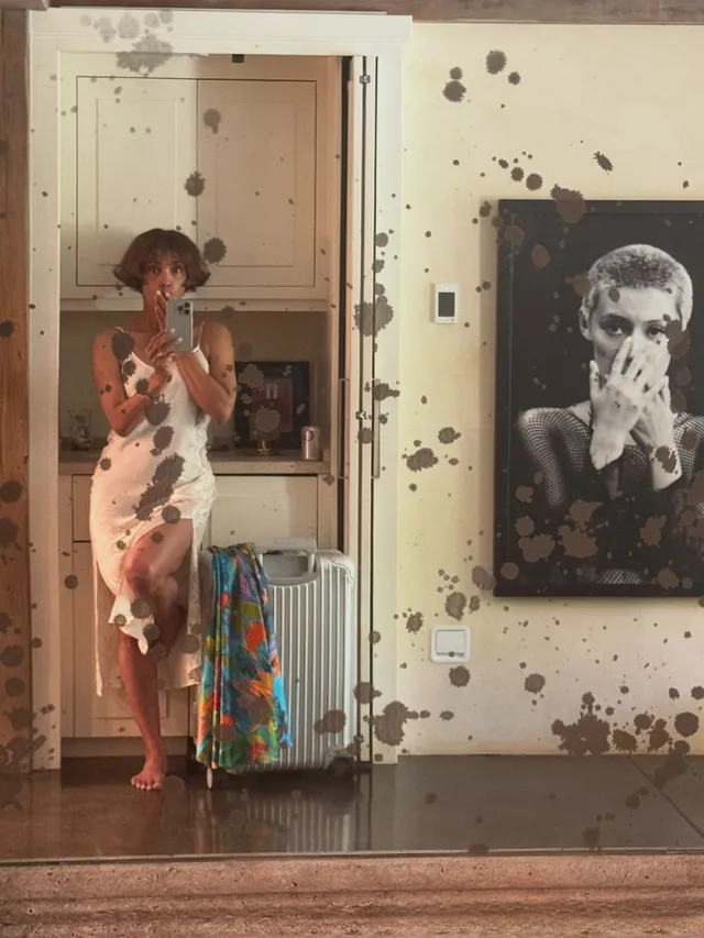 Halle Berry standing barefoot indoors in a white dress.