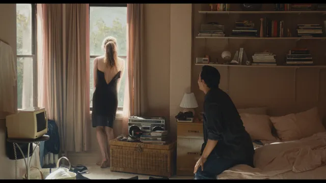 Sarah Pidgeon standing near a window in a black dress in a screen capture.