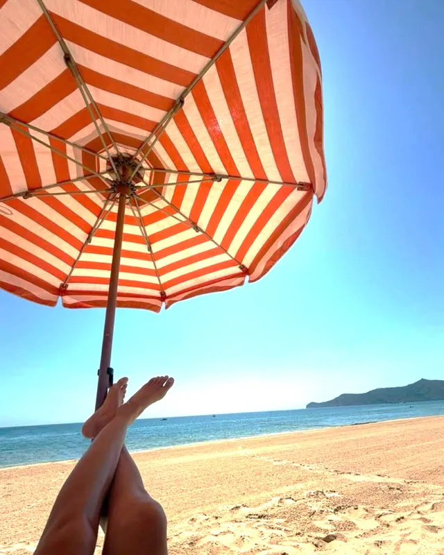 Irina Shayk bare feet beneath a striped beach umbrella.