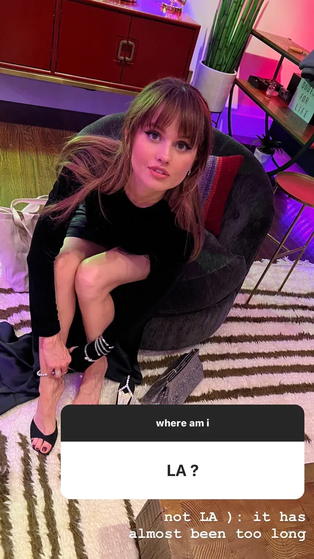 Debby Ryan sitting in a black outfit indoors.