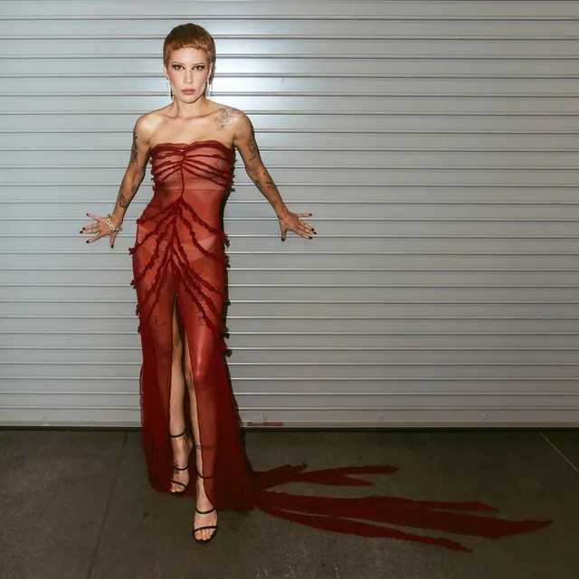 Halsey a red dress and heels beside a grey backdrop.