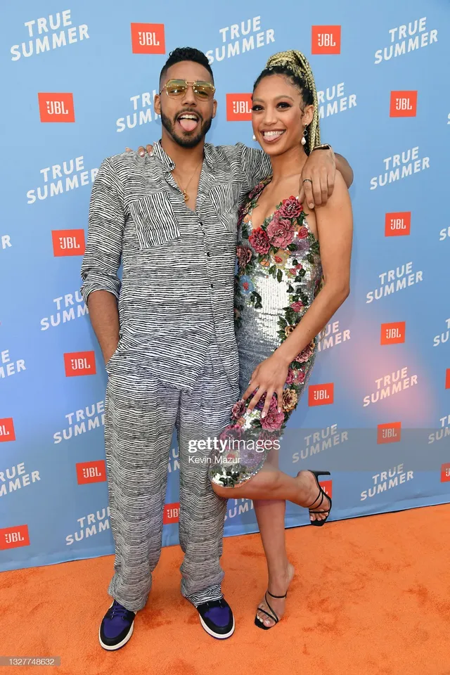 Samantha Logan lifting one foot while posing beside a man in a floral dress and heels.