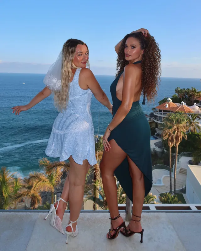 Madison Pettis posing with a friend on a terrace in a dark dress and black heels.