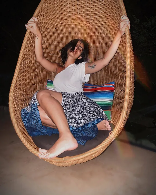 María Gabriela de Faría sitting barefoot in a hanging wicker chair.