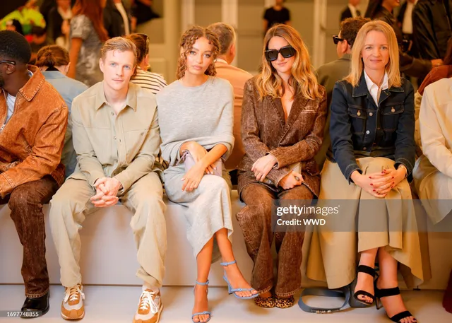 Nico Parker sitting with a group at an event in a gray dress and heels.