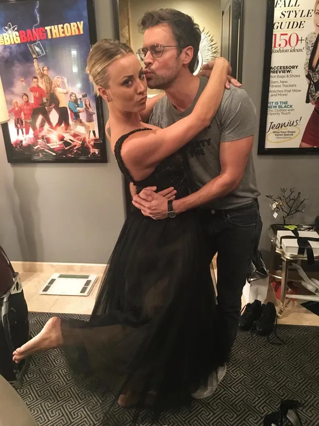 Kaley Cuoco hugging another person in a black dress with a bare foot raised.