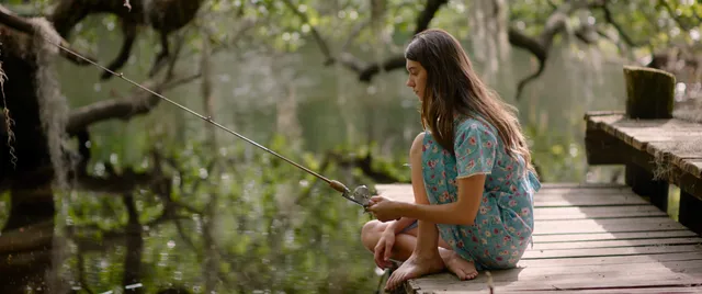Daisy Edgar-Jones seated on a wooden lakeside walkway in a screen scene.