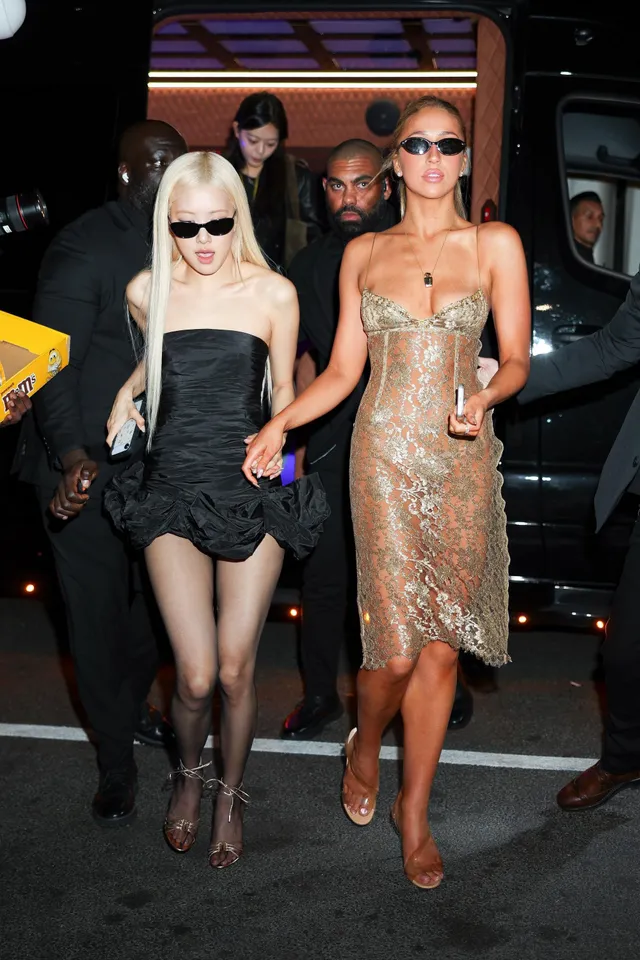 Rosé walking beside another guest at night in a short black dress and patterned heels.