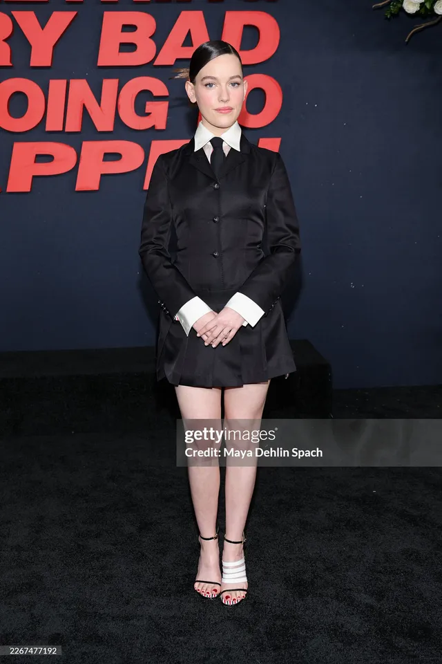 Victoria Pedretti standing at a premiere in a dark tailored outfit.