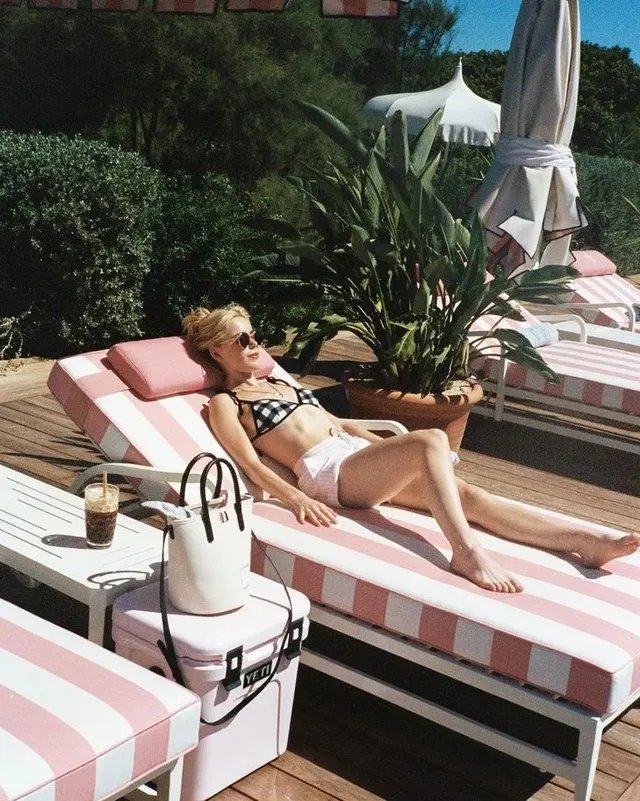 Kiernan Shipka reclining barefoot on a striped poolside lounger.