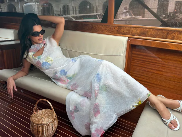 Kendall Jenner reclining on a boat in a dress and white sandals.
