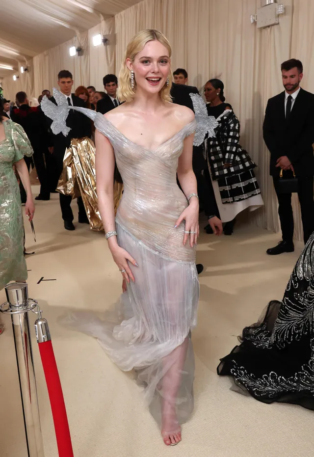 Elle Fanning walking barefoot indoors in a pale embellished gown.