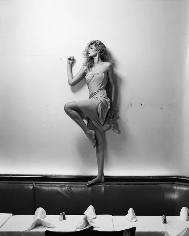 Gigi Hadid posing barefoot on a dark seat for a monochrome portrait.