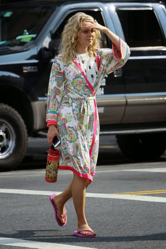 AnnaSophia Robb walking beside a vehicle in a patterned robe and flip-flops.