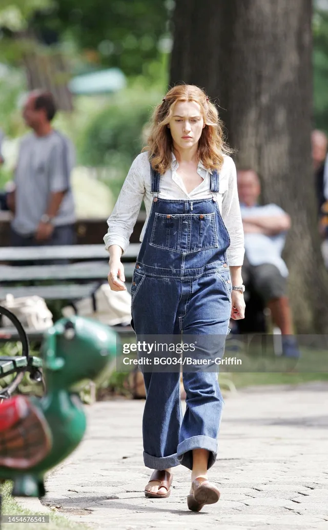 Kate Winslet walking outdoors in denim overalls and sandals.