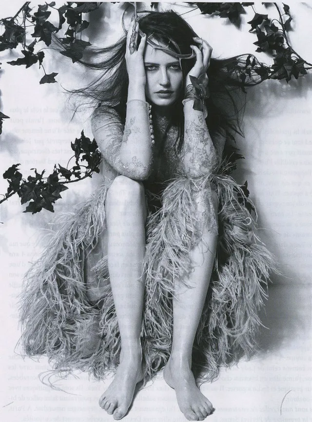 Eva Green sitting barefoot in a textured outfit for a black and white portrait.