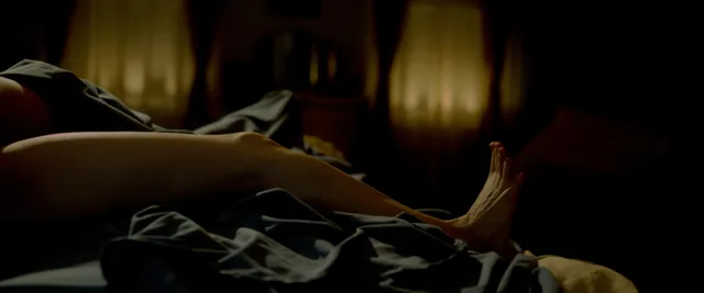 Jessica Chastain reclining on a bed in a dimly lit screen scene.