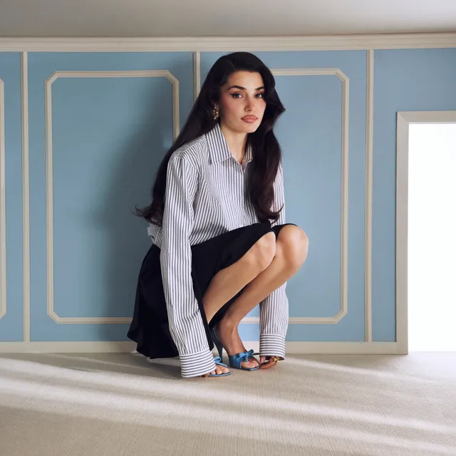 Hande Erçel crouching in a striped shirt and blue heels.