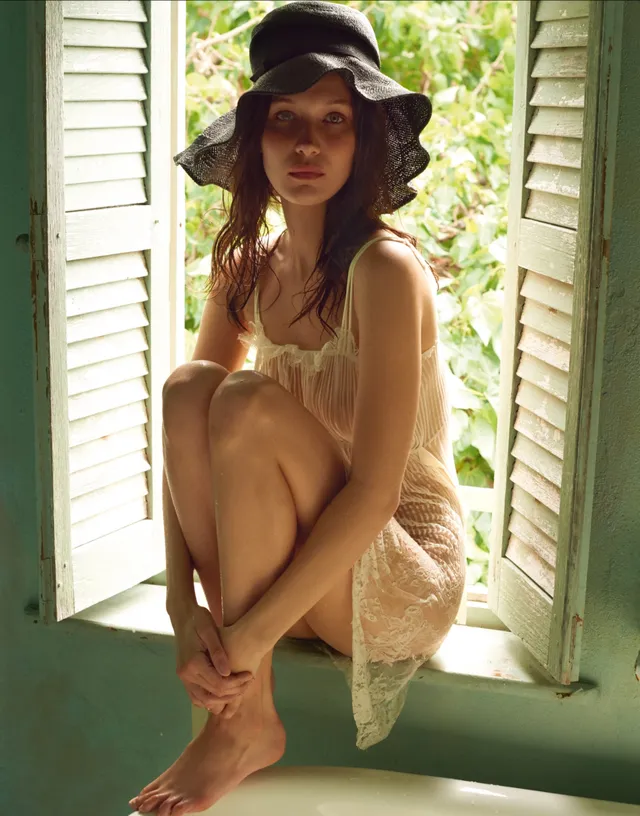 Bella Hadid sitting barefoot in a window for a portrait.