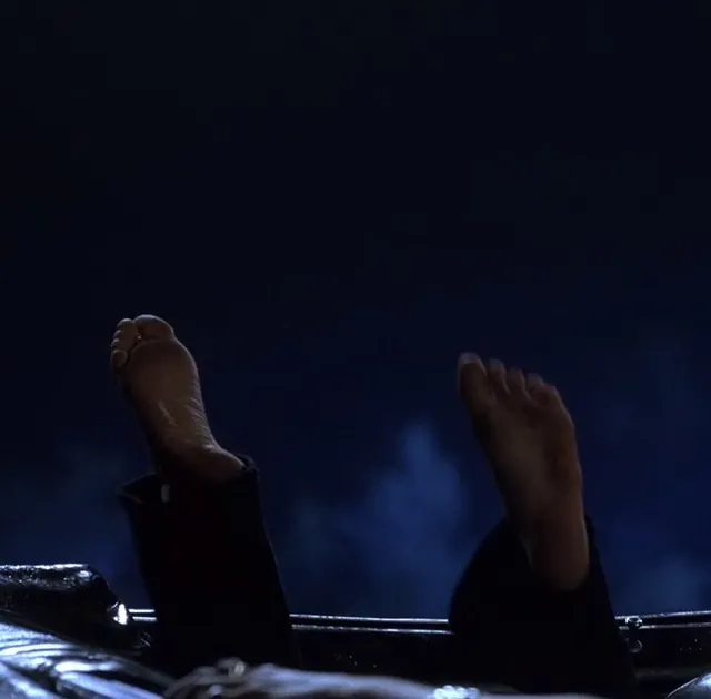 Anne Hathaway raising bare soles in a dark screen scene.