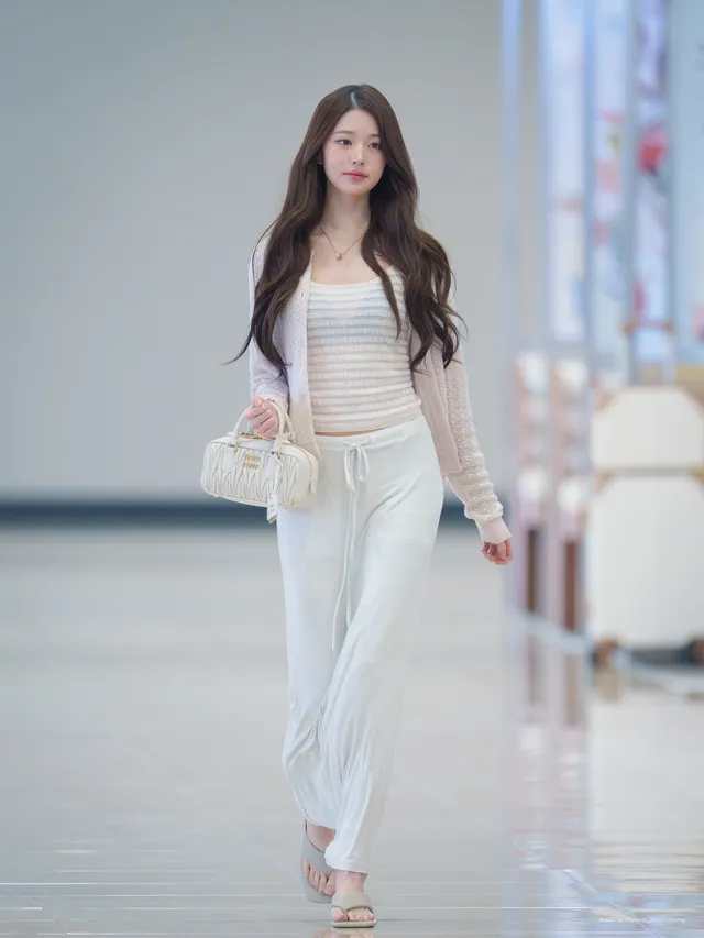 Jang Wonyoung walking indoors in a pale outfit and metallic heels.