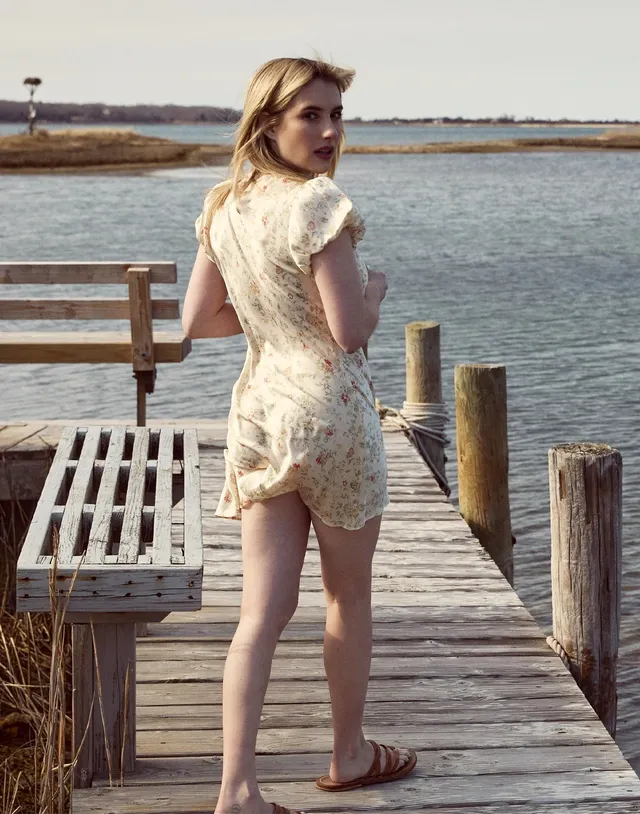 Emma Roberts standing on a wooden pier in a lace outfit and flat sandals.