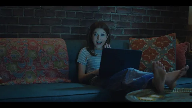 Anna Kendrick using a laptop on a sofa with bare soles facing forward.